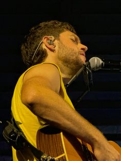 a man in yellow shirt playing an acoustic guitar with microphone and sound board behind him