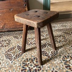 an old wooden stool sitting on top of a tiled floor