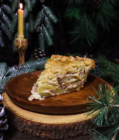 a piece of pie sitting on top of a wooden plate next to pine cones and candles