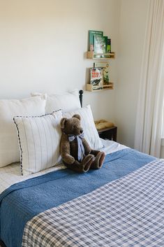 a teddy bear sitting on top of a blue and white bedspread in a bedroom