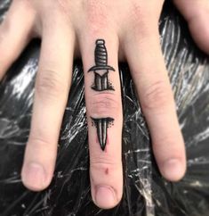 a person with a knife tattoo on their ring finger and the other hand is holding an object