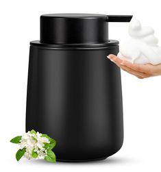 a hand is holding a white object in front of a black container with flowers on it