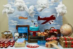 a table topped with lots of cakes and desserts next to a wall covered in clouds