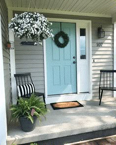 two chairs sitting on the front porch of a house with a blue door and wreath