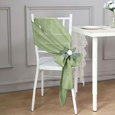 a chair with a green bow on it next to a white table and flower vase