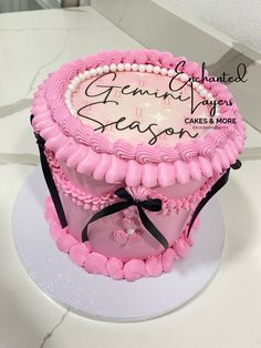 a pink cake with black ribbon and name on it sitting on a white counter top