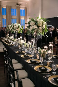 a long table is set with black linens and gold place settings for dinner guests