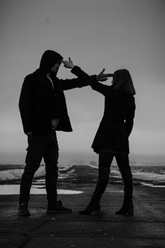 a man and woman standing next to each other in front of the ocean with their hands together