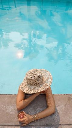 a woman sitting on the edge of a swimming pool with her hat over her head