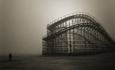 a man standing in front of an abandoned roller coaster on a foggy, overcast day