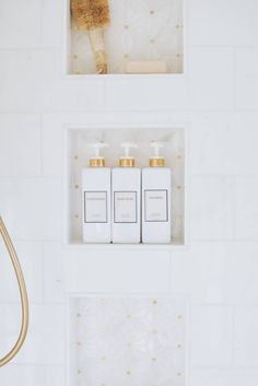 three bottles of shampoo sitting on top of a white shelf next to a shower head