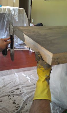 a man holding a large piece of wood on top of a hard surface covered in plastic