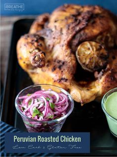 a roasted chicken with red onions and green sauce on a black tray next to a small bowl of dressing