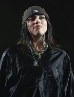 a woman with long hair wearing a black shirt and hat, standing in front of a dark background