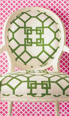 a white chair sitting in front of a wall with pink and green designs on it