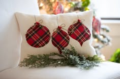 three ornaments are hanging from the back of a pillow on a white chair in front of a christmas tree