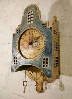 a blue and gold clock hanging from the side of a white wall with keys attached to it