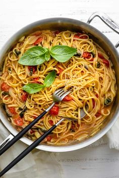 a pan filled with pasta and basil on top of a white table