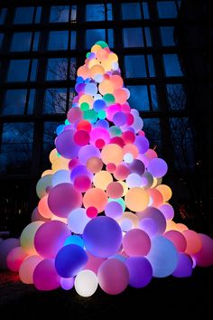 a large christmas tree made out of balloons in front of a building at night with the lights turned on