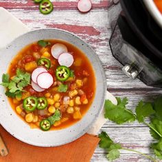 a white bowl filled with vegetable soup next to a wooden cutting board and utensils