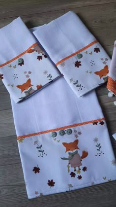 four folded napkins with foxes and leaves on them, sitting on a wooden floor