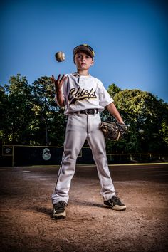 a young baseball player throwing a ball on top of a field in front of trees