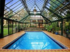 an indoor swimming pool with tiled flooring and glass walls, surrounded by greenery