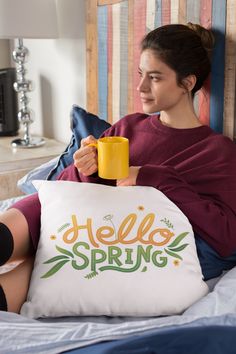 a woman sitting on her bed holding a coffee mug and reading a pillow with the word harry potter printed on it