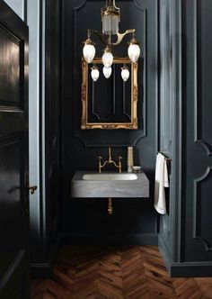 an image of a bathroom with black walls and gold accents on the mirror above the sink