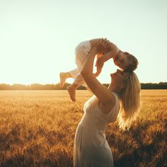 a woman holding a baby in her arms while standing in a wheat field at sunset