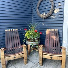 two wooden chairs sitting next to each other in front of a blue house with a wreath on the wall