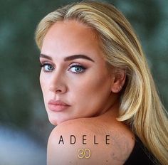 a woman with long blonde hair and blue eyes looks at the camera while wearing an adelle tattoo on her arm