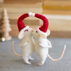 two white mice with red hats on their heads are standing next to each other in front of a christmas tree