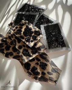 four pieces of animal print fabric with black beads on them, sitting on a white surface