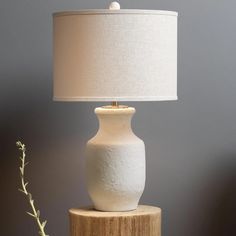 a white vase sitting on top of a wooden table next to a lampshade