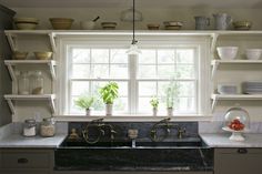 a kitchen sink under a window next to shelves with dishes on it and plants in the window sill