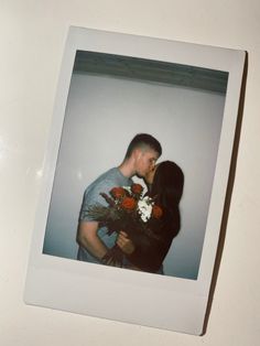 a man and woman standing next to each other in front of a white wall holding flowers