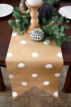 the table is decorated with white polka dot paper and pumpkins on it, along with greenery