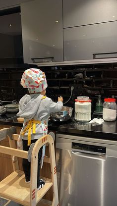 a little boy that is standing up on a ladder in the kitchen with some food