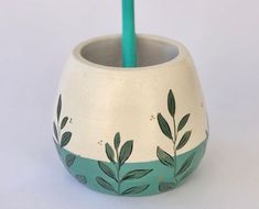 a white vase with green leaves painted on it and a blue toothbrush holder in the middle