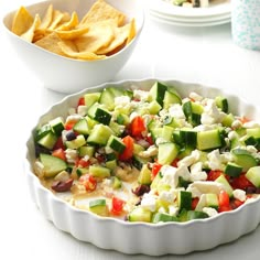 a white dish filled with cucumber, cheese and other food on a table