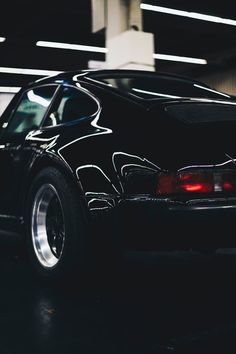 the back end of a black sports car parked in a parking garage with its lights on