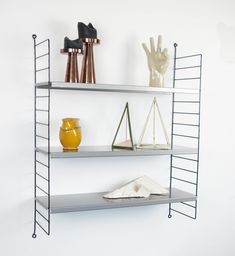 two metal shelves with books, vases and other items on them against a white wall