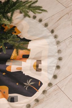 a christmas tree skirt with pom poms on the floor next to a potted plant