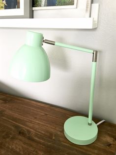 a green desk lamp sitting on top of a wooden table next to a framed picture