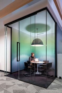 a person sitting at a table in an office with glass walls and round lights hanging from the ceiling