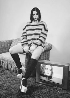 a woman sitting on top of a couch in front of a tv with her legs crossed