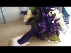 a bridal bouquet with purple and white flowers is being held by someone's hand