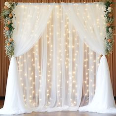 a decorated stage with white drapes and flowers on the top, surrounded by fairy lights