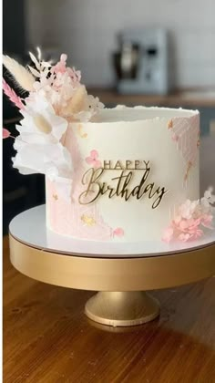 a white and pink birthday cake sitting on top of a wooden table